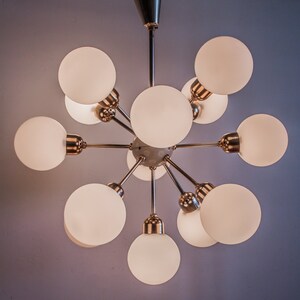 May include: A gold-toned chandelier with 10 white frosted glass globes. The chandelier has a starburst design with the globes extending outward from a central point.