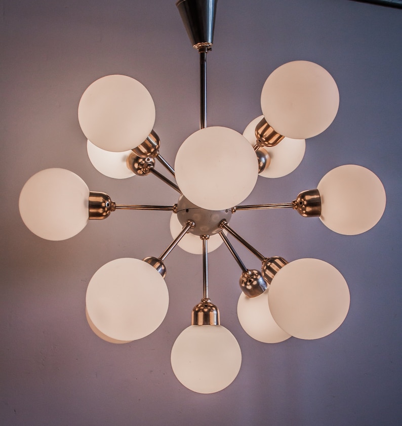 May include: A gold-toned chandelier with 10 white frosted glass globes. The chandelier has a starburst design with the globes extending outward from a central point.