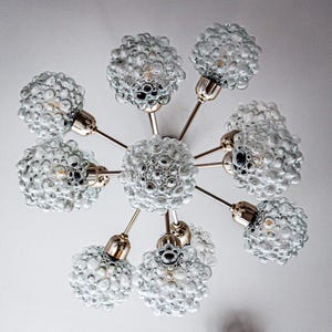 May include: A brass and glass chandelier with eight bubbled glass shades. The chandelier has a starburst design with the shades extending out from a central point.