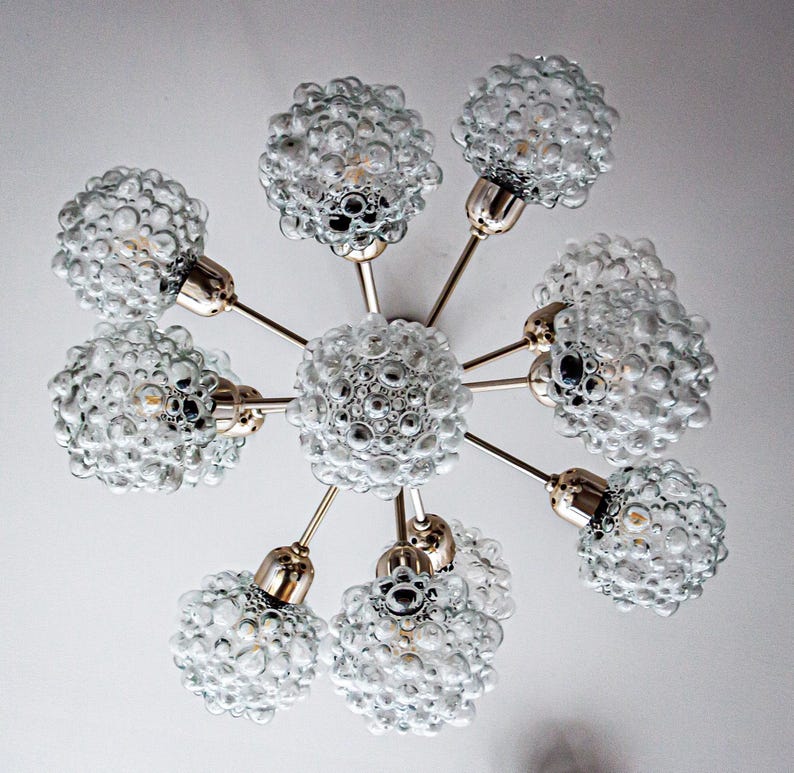 May include: A brass and glass chandelier with eight bubbled glass shades. The chandelier has a starburst design with the shades extending out from a central point.