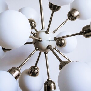 May include: A white and gold mid-century modern chandelier with multiple globe-shaped light fixtures.