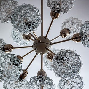 May include: A brass and glass chandelier with eight light bulbs. The glass shades are clear and have a bubbled texture.