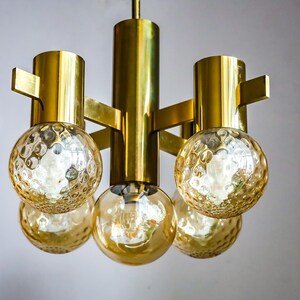 May include: A gold-toned chandelier with five round, textured glass shades. The chandelier has a modern design with a geometric frame.