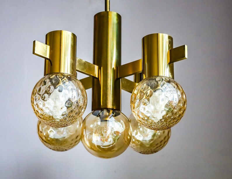 May include: A gold-toned chandelier with five round, textured glass shades. The chandelier has a modern design with a geometric frame.