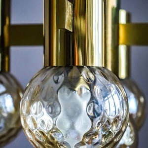 May include: A brass and glass chandelier with six textured glass globes. The chandelier has a modern design and would be a great addition to any home.