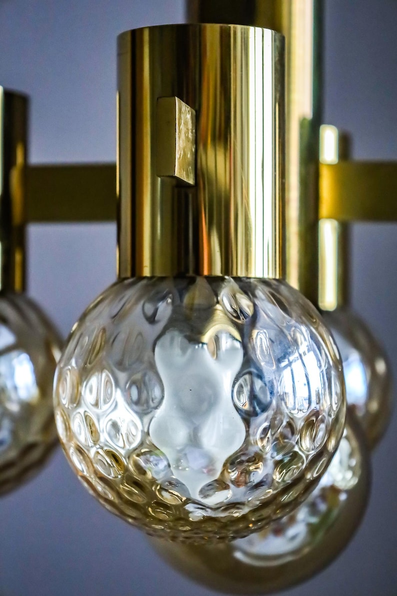 May include: A brass and glass chandelier with six textured glass globes. The chandelier has a modern design and would be a great addition to any home.