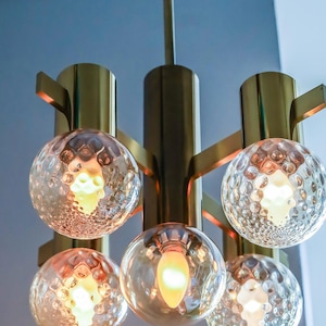 May include: A brass and glass chandelier with five light bulbs. The chandelier has a modern design with a geometric shape and clear glass globes.