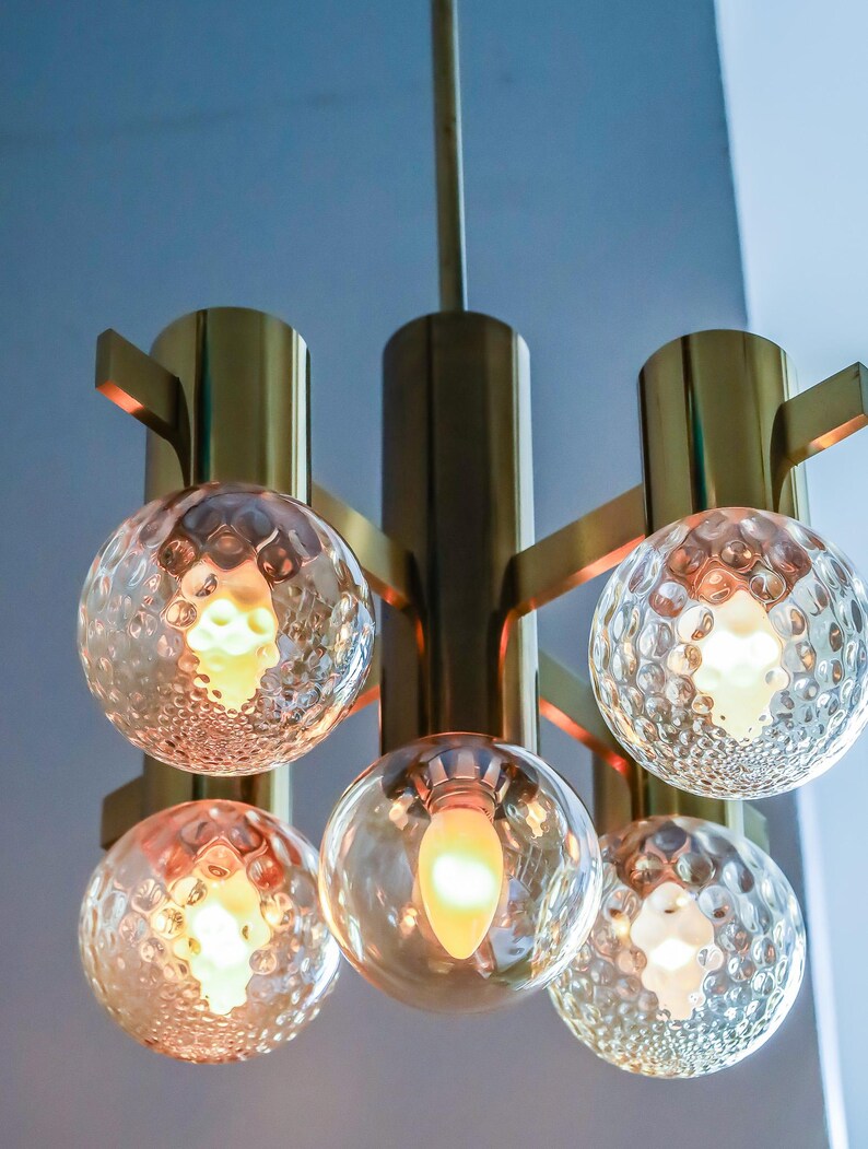 May include: A brass and glass chandelier with five light bulbs. The chandelier has a modern design with a geometric shape and clear glass globes.