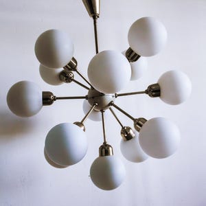 May include: A white, multi-light chandelier with a brass finish and a starburst design. The chandelier has 10 round, white glass shades.