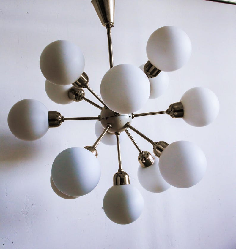May include: A white, multi-light chandelier with a brass finish and a starburst design. The chandelier has 10 round, white glass shades.
