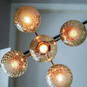May include: A gold metal chandelier with five round, textured glass globes. Each globe has a warm white light bulb inside.
