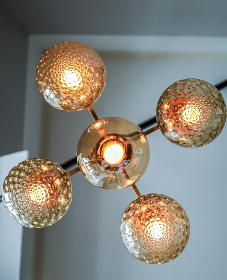 May include: A gold metal chandelier with five round, textured glass globes. Each globe has a warm white light bulb inside.