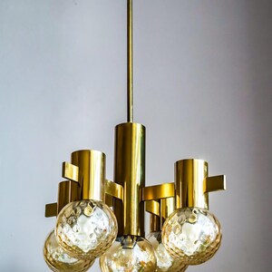 May include: A gold-toned chandelier with five round, textured glass shades. The chandelier has a simple, modern design.