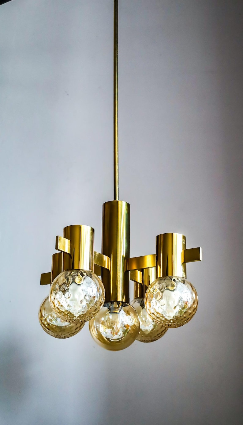 May include: A gold-toned chandelier with five round, textured glass shades. The chandelier has a simple, modern design.