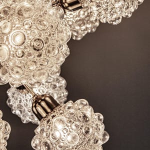May include: Close-up of a chandelier with multiple clear glass globes. Each globe has a textured surface with small bubbles. The globes are attached to a silver metal frame.