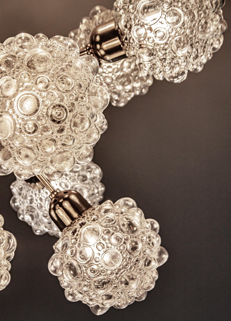 May include: Close-up of a chandelier with multiple clear glass globes. Each globe has a textured surface with small bubbles. The globes are attached to a silver metal frame.