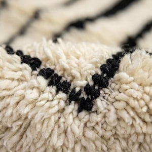 May include: A thick, high-pile rug featuring a cream-colored base with distinct, dark black horizontal stripes. The texture is composed of dense, soft fibers that create a deep, shaggy appearance, highlighting the contrast between the light and dark yarns.
