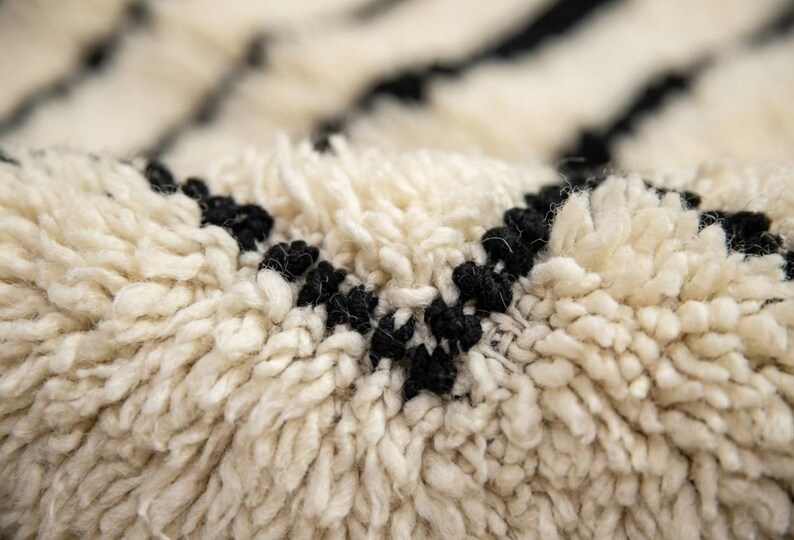 May include: A thick, high-pile rug featuring a cream-colored base with distinct, dark black horizontal stripes. The texture is composed of dense, soft fibers that create a deep, shaggy appearance, highlighting the contrast between the light and dark yarns.