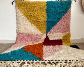 May include: A colorful geometric rug with a white, pink, yellow, orange, blue, and red design. The rug has a fringe border.
