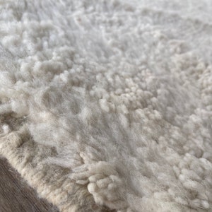 May include: Close-up of a white, fluffy rug with a beige border. The rug has a textured, hand-woven look.