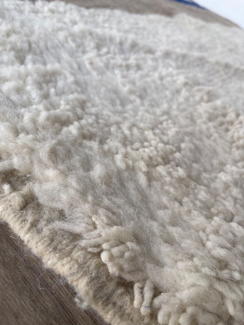 May include: Close-up of a white, fluffy rug with a beige border. The rug has a textured, hand-woven look.