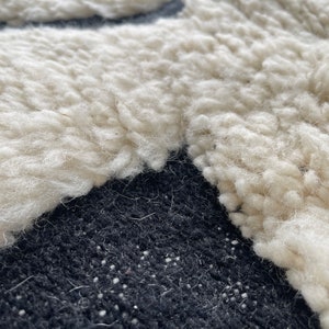 May include: Close-up of a white fluffy rug with a black background. The rug has a unique texture and is made of soft, plush fibers.