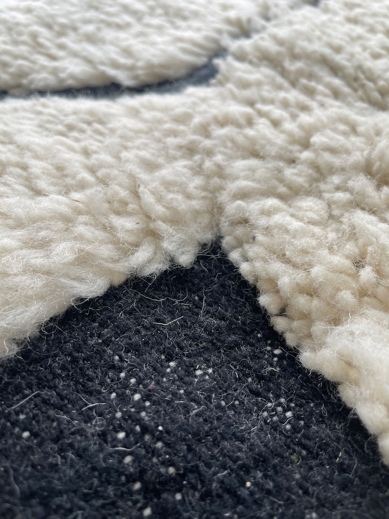 May include: Close-up of a white fluffy rug with a black background. The rug has a unique texture and is made of soft, plush fibers.