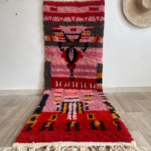 May include: A long, rectangular rug with a pink, red, black, and yellow geometric pattern. The rug has a fringe on the bottom.
