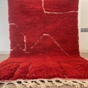 May include: A vibrant red, textured rug with a geometric design. The rug features a mountain-like pattern in white, with a fringe along the bottom edge. The thick pile suggests a soft, comfortable texture, suitable for a living room or bedroom.