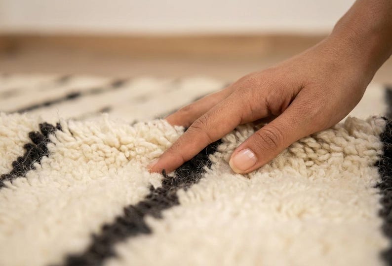 May include: A thick, cream-colored shag rug featuring bold, dark charcoal-gray horizontal stripes. The rug has a deep, plush pile texture with long, soft fibers that create a dense and cozy surface appearance across the entire woven textile.