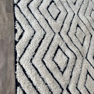May include: A white and black geometric patterned rug with a thick, fluffy texture. The rug has a diamond pattern with black lines.