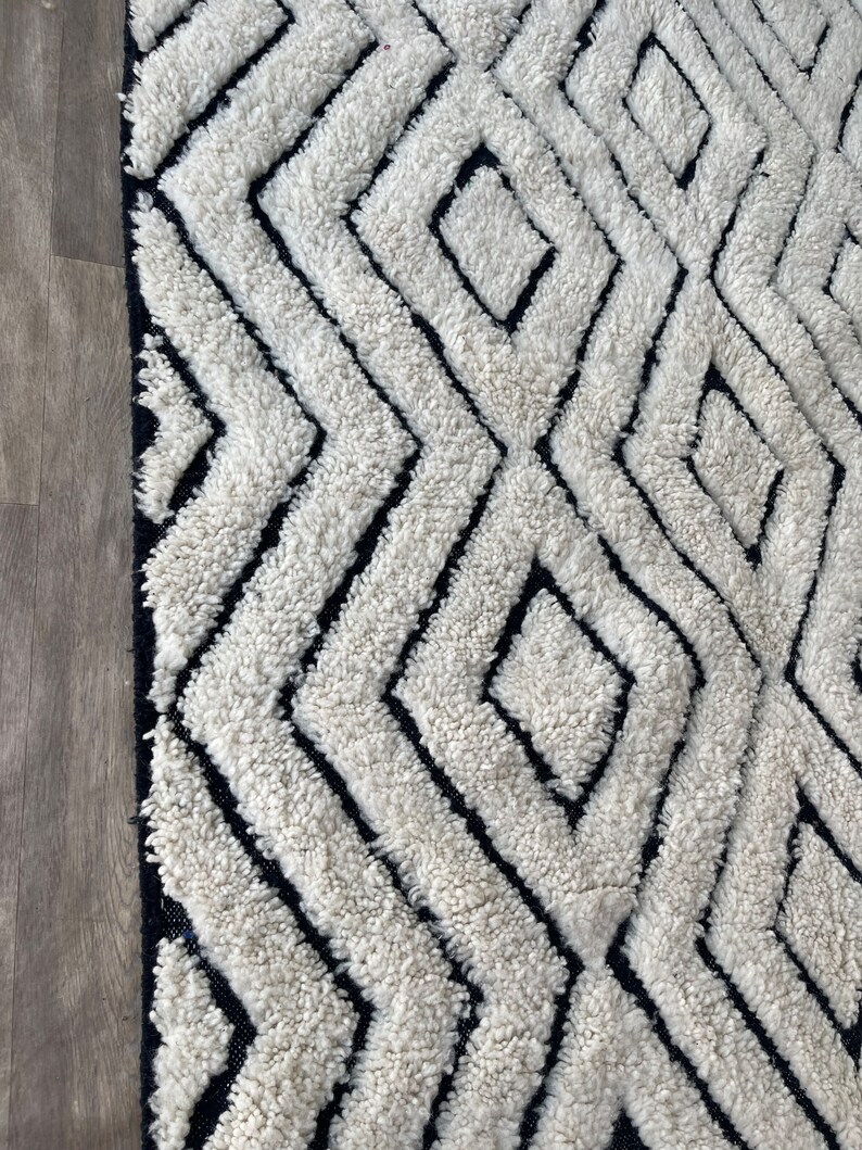 May include: A white and black geometric patterned rug with a thick, fluffy texture. The rug has a diamond pattern with black lines.