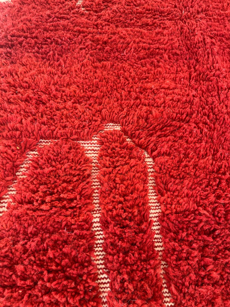 May include: Close-up of a vibrant red, textured rug with a shaggy pile. The rug features a pattern of white vertical stripes against the red background, creating a bold contrast. The thick, plush texture suggests a comfortable and cozy feel.