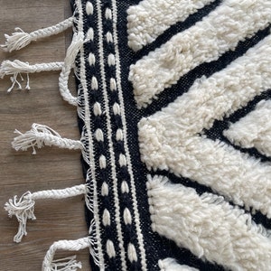 May include: Black and white rug with a geometric pattern and fringe. The rug is made of a thick, fluffy material.