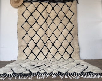 May include: A white and black Moroccan rug with a diamond pattern. The rug has a fringe border.