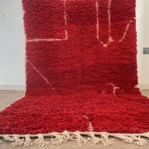 May include: A vibrant red rug with a thick, textured pile. The rug features a geometric design in white, with a fringe along the bottom edge. The rug is a decorative floor covering.