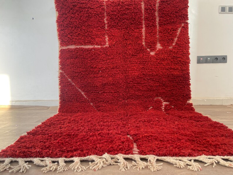 May include: A vibrant red rug with a thick, textured pile. The rug features a geometric design in white, with a fringe along the bottom edge. The rug is a decorative floor covering.