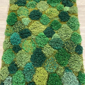 May include: A rectangular rug with a textured, tufted design in various shades of green. The rug features a pattern of raised, rounded shapes, creating a three-dimensional effect. The colour palette ranges from light to dark greens.