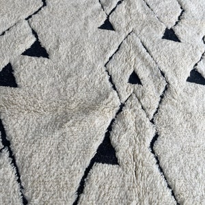 May include: A white and black geometric patterned rug with a fluffy texture. The rug has a diamond pattern with black triangles inside each diamond.