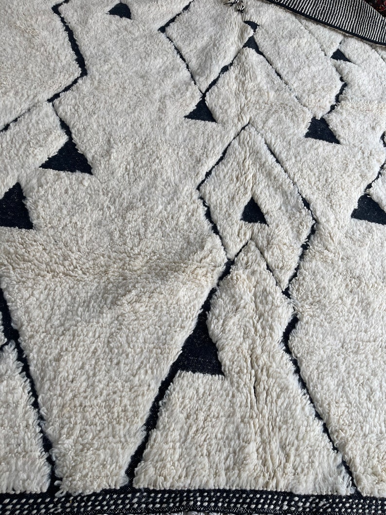 May include: A white and black geometric patterned rug with a fluffy texture. The rug has a diamond pattern with black triangles inside each diamond.