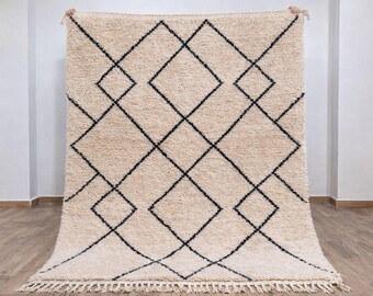 May include: A rectangular area rug with a thick, cream-colored wool pile featuring a dark charcoal geometric diamond pattern. The rug has a knotted fringe along the bottom edge and a symmetrical grid design across the entire surface.