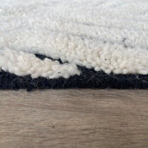 May include: Close-up of a white and black rug with a fluffy texture. The rug has a black border and is made of wool.
