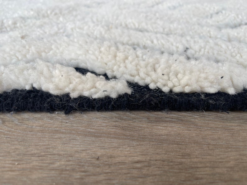 May include: Close-up of a white and black rug with a fluffy texture. The rug has a black border and is made of wool.