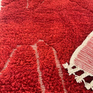 May include: A close-up of a vibrant red, shaggy rug with a textured surface. The rug has a geometric design with white stripes. A smaller rug with white tassels is visible in the corner.