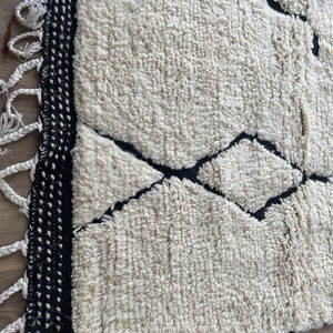 May include: A white and black Moroccan rug with a geometric pattern. The rug has a fringe border and is made of wool.