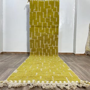 Könnte beinhalten: Ein langer, schmaler Teppich mit einem geometrischen Muster in Gelb- und Weißtönen. Der Teppich hat an beiden Enden Fransen.