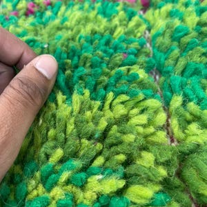 Pu&ograve; includere: Primo piano di un tappeto verde e rosa con una texture soffice. Il tappeto &egrave; fatto di lana e ha un design unico tessuto a mano.