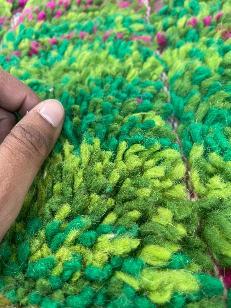 Pu&ograve; includere: Primo piano di un tappeto verde e rosa con una texture soffice. Il tappeto &egrave; fatto di lana e ha un design unico tessuto a mano.