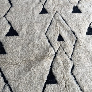 May include: A white and black geometric patterned rug with a fluffy texture. The rug features a repeating pattern of diamonds and triangles.