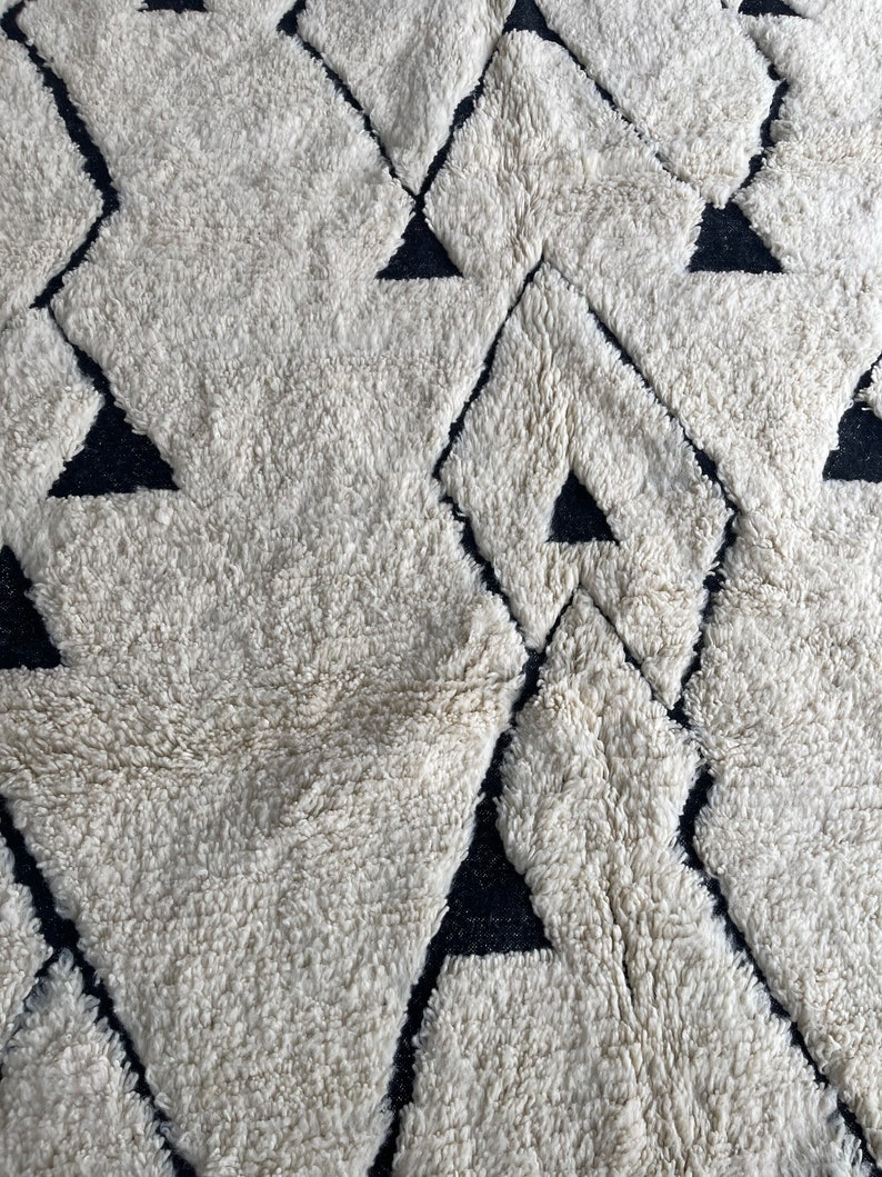 May include: A white and black geometric patterned rug with a fluffy texture. The rug features a repeating pattern of diamonds and triangles.